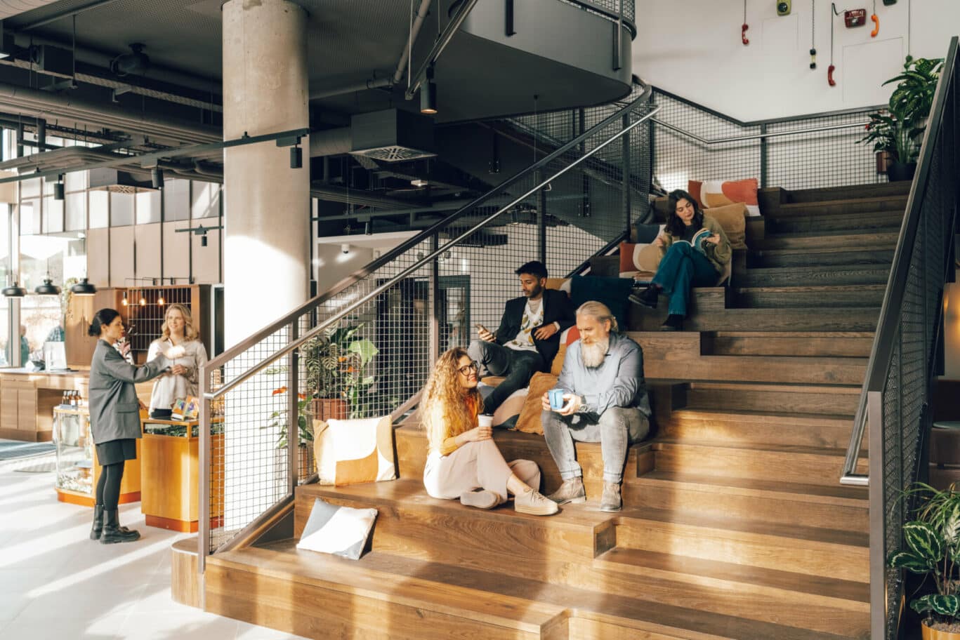 Treppe im Eingangsbereich des Revo Hotel München. Gäste sitzen auf dieser und sprechen miteinander oder lesen ein Buch.